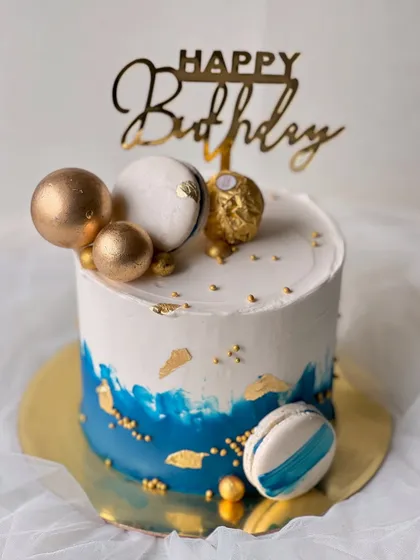 A stylish and masculine design perfect for him. This rich vanilla buttercream cake features a blue watercolor effect, gold leaf, macarons, and a Ferrero Rocher topper.