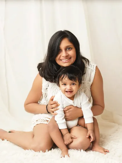 A mother and her baby boy share a happy moment. The simple white background and casual outfits make this feel like a natural, candid family photo.