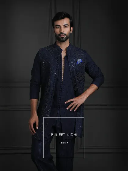 This outfit is an expression of legacy. A navy open jacket with detailed geometric embellishments, complemented by a loop-buttoned tunic and textured bell-bottom lowers.