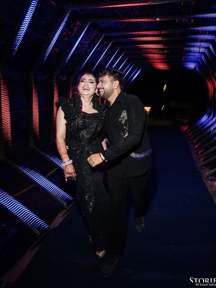 A candid shot of the couple laughing as they walk through a colorful, lit-up tunnel at their reception.
