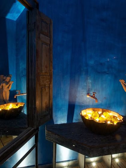 Another view from our archives of 'The Big Door'. This space uses deep blue textured walls and antique wooden elements to create a dramatic, moody atmosphere. The warm, focused lighting highlights traditional sculptures, blending heritage with contemporary design.