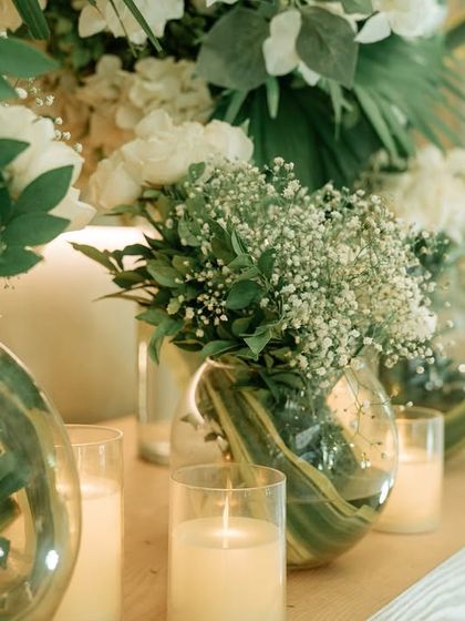 A close-up of the simple yet beautiful arrangements of baby's breath and white roses in glass vases, surrounded by the warm glow of candles.
