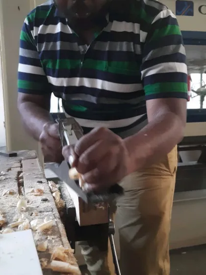 A student learns to use a hand plane to smooth and flatten a piece of wood, creating a perfectly finished surface by hand.