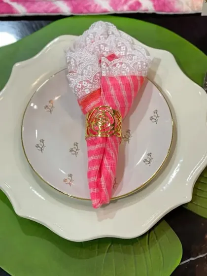 A vibrant pink and white patterned napkin is elegantly held by a golden floral ring. This shows how a simple accessory can tie together different colors and textures in your tablescape.
