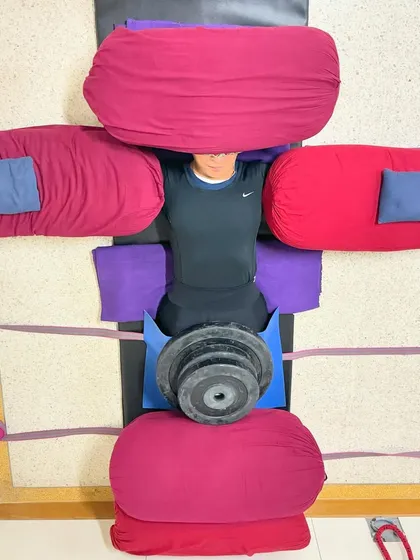 This is a fully supported Savasana, sometimes called 'the human cross.' The arrangement of bolsters and weights grounds the body, opens the chest, and quiets the mind, leading to a state of complete surrender and deep rest.