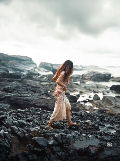 A wide shot of the model walking on the dark, volcanic-looking rocks. The contrast between the sparkling dress and the dark, dramatic landscape is incredibly powerful.