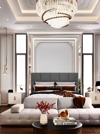 A grand and symmetrical master bedroom with high ceilings and classic wall paneling. The design includes a large statement chandelier and a seating area at the foot of the bed, exuding timeless elegance.