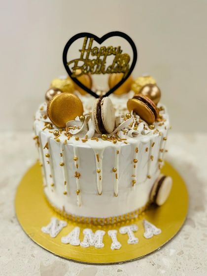 A shimmering white and gold drip cake, topped with golden macarons and a heart topper.
