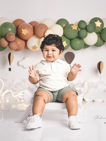 A happy one-year-old boy in a hot air balloon themed setup. His smile is as bright as the stars on the balloons.