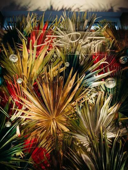A detail shot of the tropical decor for a 20th birthday. The lush arrangement of dried and fresh leaves, combined with moody lighting and a neon sign, creates a sophisticated and trendy party vibe.