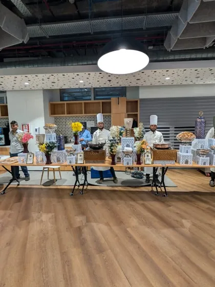 This wide shot showcases the full scale of our catering setup within a modern office cafeteria. The long buffet table is staffed by our chefs in uniform, ready for the Hogarth 500-strong celebration to begin.