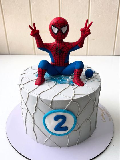 A friendly neighborhood Spider-Man cake for a second birthday. This design features a gray web-covered tier topped with a cheerful, hand-sculpted Spidey figure, ready for action.