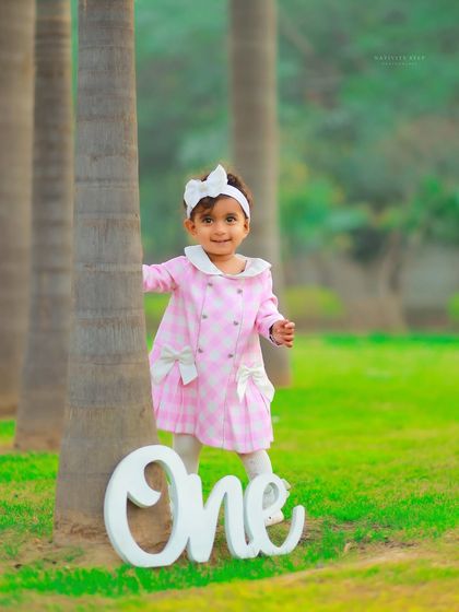 A classic first birthday portrait in the park. This little girl's adorable pink coat and the simple "One" prop make for a sweet and timeless memory of her turning one.