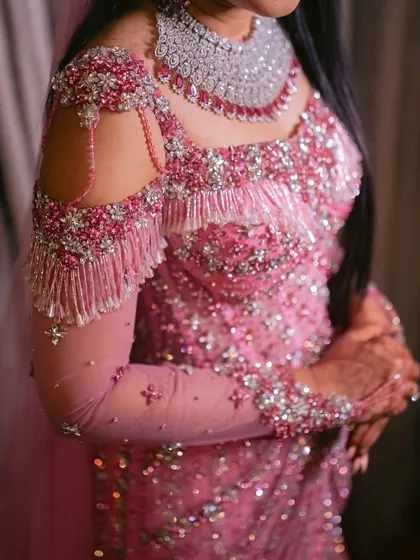 A close up of the cold shoulder detail on a modern bridal gown. Cascading beadwork and shimmering tassels add movement and a touch of playful glamour to the structured bodice.