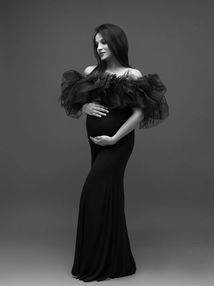 A solo portrait in black and white, emphasizing the elegant silhouette of the mom-to-be and the dramatic texture of her gown.