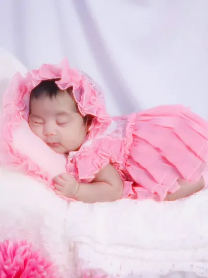 Another angle of the baby girl in her pink dress, resting on a soft white pillow. We take multiple shots to ensure we get the perfect portrait.
