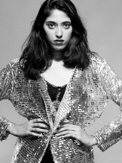 A striking black and white editorial portrait. The model wears a transparent sequin jacket, creating a bold, high-fashion look with a strong, direct gaze.