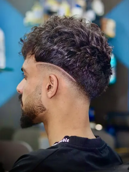 Fade today, confidence forever. This curly haircut is enhanced with a sharp, curved razor line that adds a dynamic element to the style.