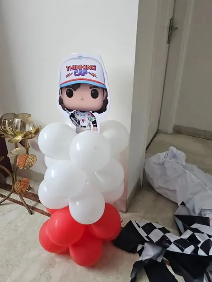 A close-up of a 'Stranger Things' character cutout on a red and white balloon pillar, showing a small detail from the larger party setup.