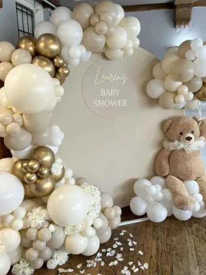 A neutral and elegant teddy bear baby shower. The theme uses a soft, creamy color palette with white and gold balloons, and a large teddy bear sitting on a cloud of balloons.