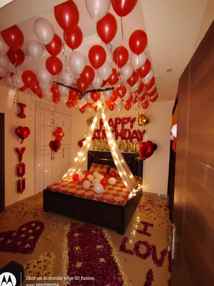 This is one of my most requested romantic birthday surprises for a husband or partner. The setup includes a fairy light canopy over the bed, red and white balloons, and 'I LOVE YOU' spelled out with rose petals on the floor.