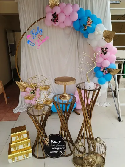 A behind-the-scenes look at a gender reveal baby shower setup, showing the pink and blue balloon arch and elegant gold-accented props.
