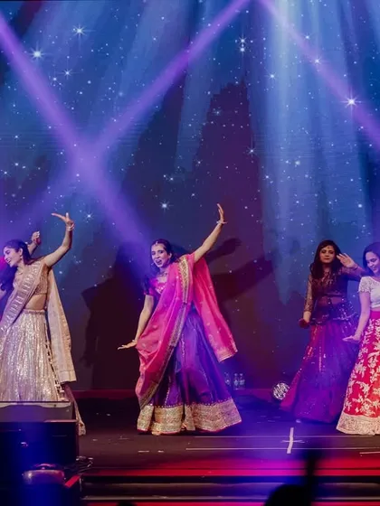 A vibrant performance by the bride and her family, with colorful outfits and synchronized moves under dramatic stage lighting.
