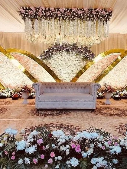 This grand reception stage uses sweeping, curved backdrops covered in thousands of flowers. The hanging floral chandelier and intricate floor patterns complete this luxurious and impressive design.