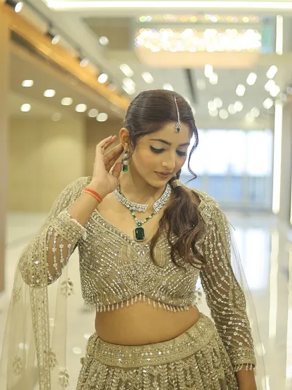 A beautiful party look featuring a shimmering gold lehenga. The makeup is kept soft and glowing, with emerald green jewellery adding a pop of colour. The focus is on radiant skin and defined eyes.