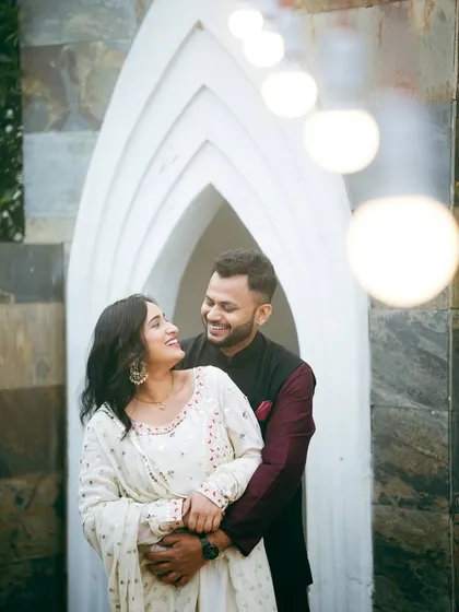 A happy, candid embrace in front of one of our unique white architectural backdrops. The string lights add a touch of warmth and magic to this pre-wedding portrait.
