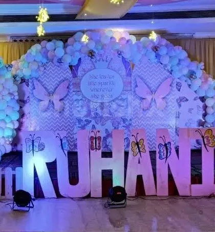A custom butterfly themed stage with large marquee letters spelling "RUHANI" and a backdrop filled with butterfly illustrations and balloons.