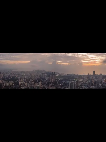 A letterboxed panoramic view of the Mumbai cityscape, emphasizing the wide, cloudy sky above.