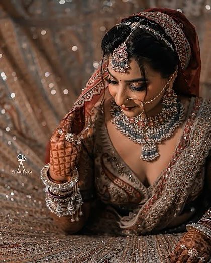 A stunning shot of a bride lying on her glittering lehenga, showcasing her complete bridal look with a heavy diamond-look necklace, maang tikka, and nath.