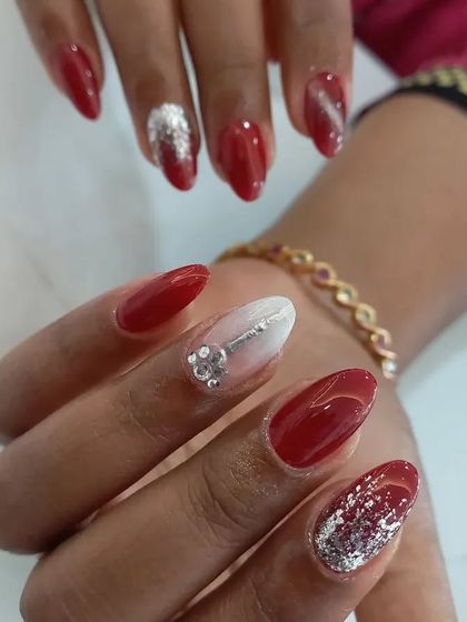 A glamorous mix of styles, including solid red, silver glitter, and a white ombré nail with a 3D silver key charm and rhinestones.
