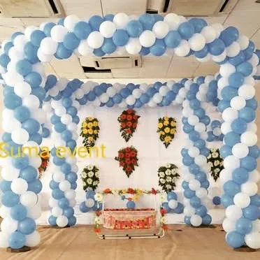 A simple and clean naming ceremony decoration using a large balloon arch in blue and white. The cradle is placed in the center with simple flower arrangements on the wall behind it.