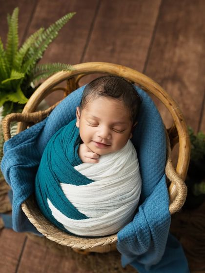 A heart-melting smile from this happy dreamer. The combination of teal and white wraps against the wooden backdrop creates a fresh and modern newborn portrait.