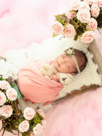 A peaceful newborn girl, swaddled in soft pink and surrounded by a bed of delicate roses. Our newborn photography sessions prioritize your baby's comfort while creating beautifully styled portraits.