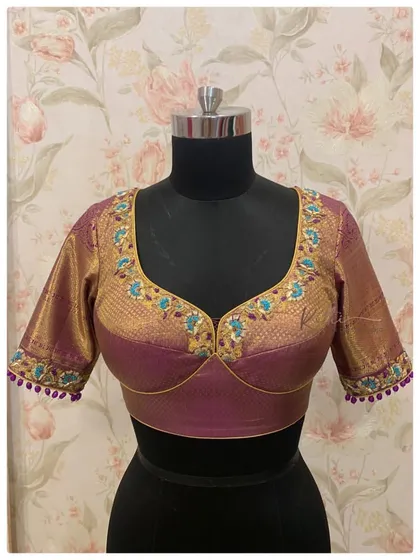 A violet silk blouse with a padded bustier cut, featuring beautiful turquoise and gold floral embroidery along the neckline.