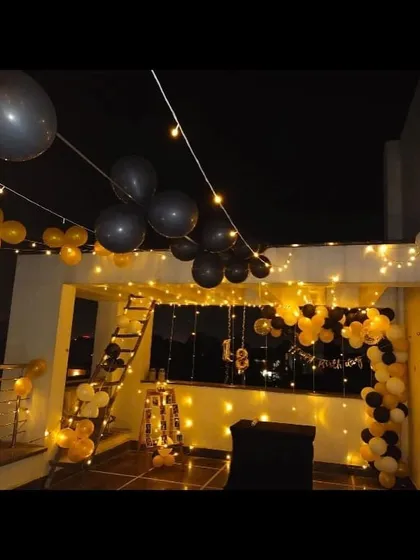 A nighttime terrace party setup with black and yellow balloons strung across the space, complemented by warm fairy lights for a festive mood.