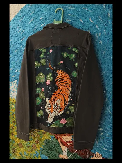 A slightly different perspective of the tiger jacket, showcasing the full back panel and the rich texture of the paint on the dark denim fabric.
