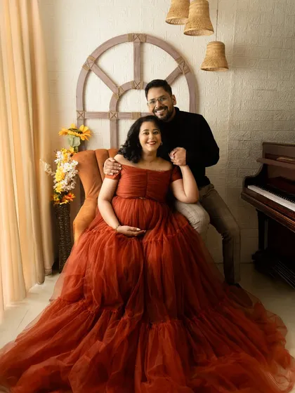 A cozy couple's portrait in a rich, rust-colored gown. The studio setting includes classic props like a piano to add a touch of timeless elegance.