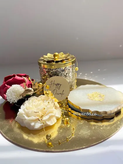 This festive gold platter is an elegant base for a Diwali gift. It features resin coasters, a decorative jar, and floral accents for a touch of luxury.