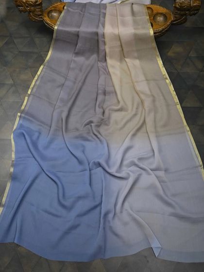 A modern ombre-dyed chiffon saree in shades of grey and blue with a thin gold border. This is a chic and understated piece for a contemporary party look.