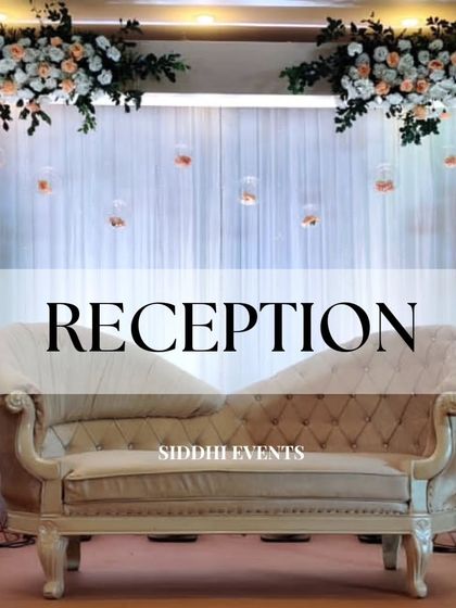 A classic reception stage setup featuring an elegant chaise lounge, a backdrop of peach and white florals, and delicate hanging glass terrariums.