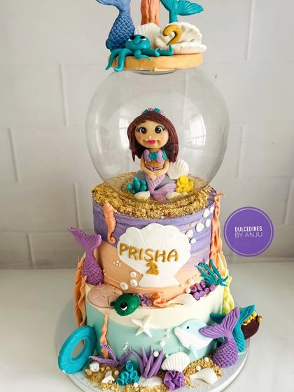 A spectacular three-tier mermaid cake featuring a mermaid figure inside a clear globe, surrounded by handcrafted sea creatures.