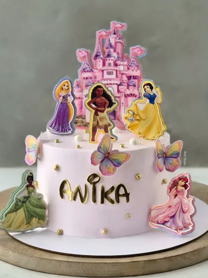 A magical Disney Princess cake featuring a castle and beloved characters like Moana, Snow White, and Ariel, all on a soft pink whipped cream base.