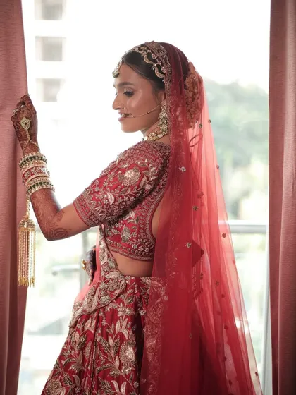 A moment of quiet reflection before the ceremony. Her dramatic eye makeup and traditional red attire create a powerful bridal statement.