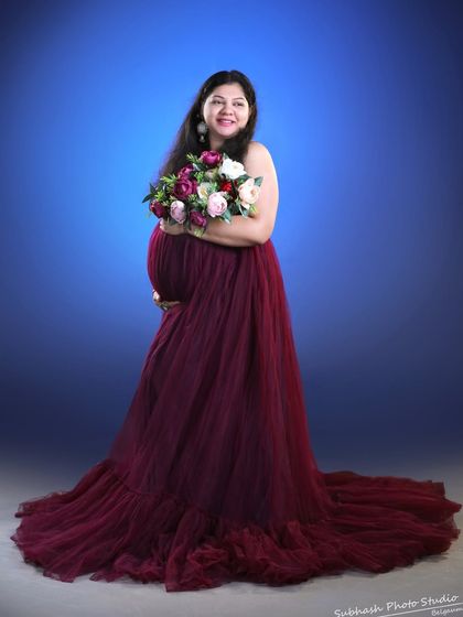 Holding a bouquet of flowers, this mom-to-be looks radiant in a wine-colored gown against a simple blue studio backdrop.