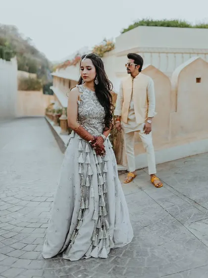 A full-length portrait of the couple, showcasing the bride's unique tassel-detailed lehenga for her Haldi event.