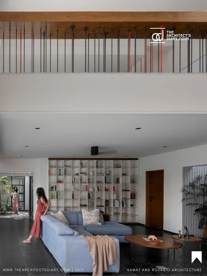 The main living area is a double-height space, visually connected to the upper floor by a simple railing. A large, open bookshelf serves as a feature wall, adding personality and storage without cluttering the minimalist design.